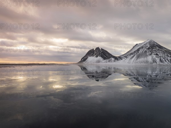 Stokksnes Beach in Iceland showcases stunning winter reflections. Snow-dusted peaks and tranquil