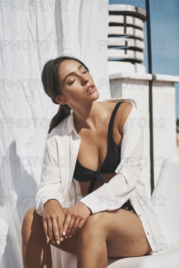 A young woman in stylish swimwear and a white shirt enjoys the summer sun on a rooftop The bright