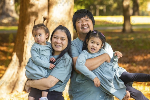 A joyful Asian family with parents and two young children, smiling and playing together in a sunny