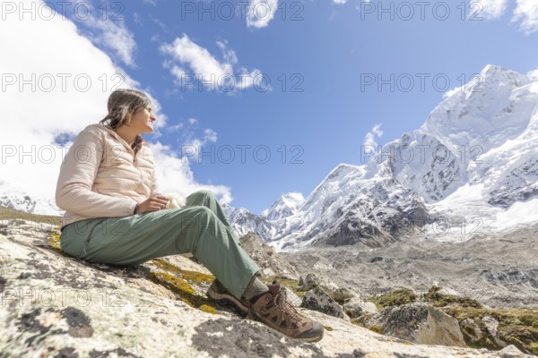 A woman sitting on a rock during a trek in the Everest region, admiring the majestic snow-capped
