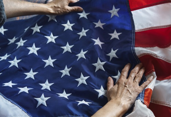 Hands gently hold the American flag, with its iconic stars and stripes. This image symbolizes