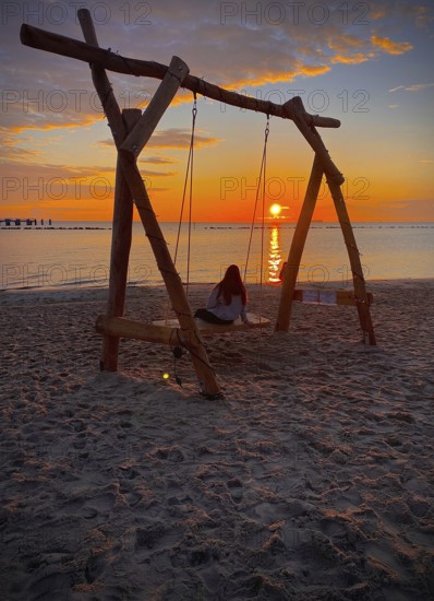 Young girl sitting on a swing on the beach watching sunrise on the island of Rügen,