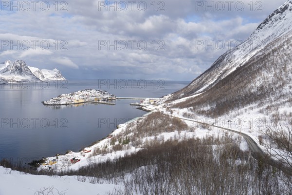 Serene winter view of Husoy, Norway, with a snow-covered coastline, calm sea, and dramatic