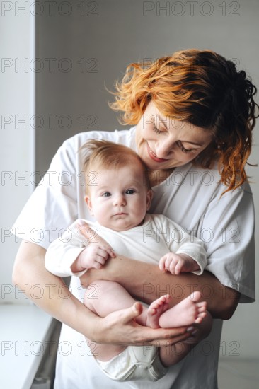 A mother lovingly holds her newborn baby girl, captured in warm natural light. The white clothing