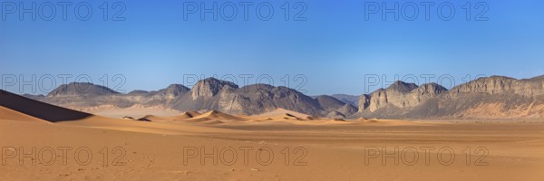 Gentle sand dunes with mountains in the background and a bright blue sky, The landscape of the
