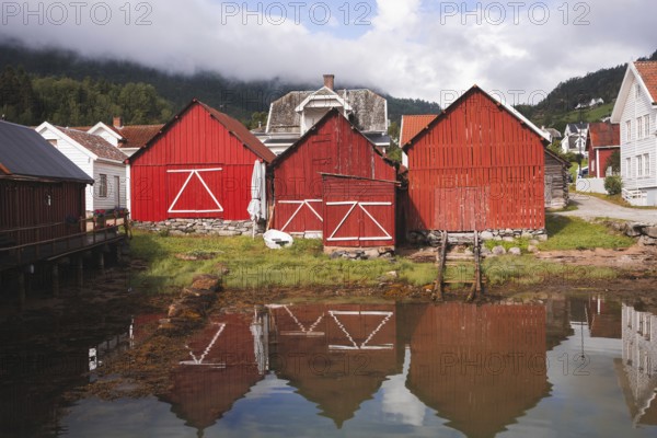 Charming red wooden huts reflect in the calm water of a Norwegian fjord village Surrounded by lush