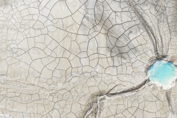 Aerial view of cracked earth with intricate lines and a vibrant blue water body in the corner. This
