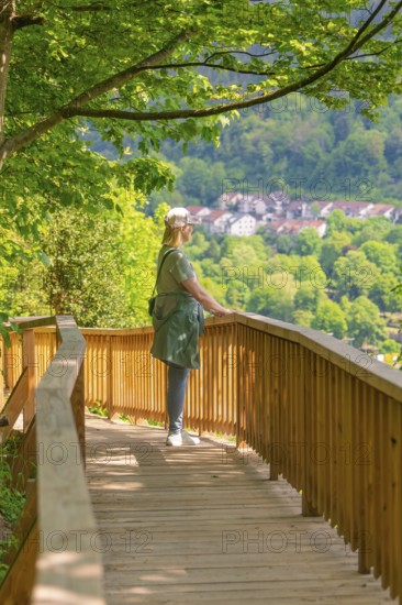 Woman on the wooden path looks at a village in the middle of a spring-like forest landscape,