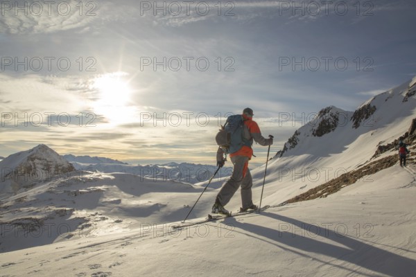 Two backcountry skiers ski down a pristine snowy mountain under a bright sky. Equipped with