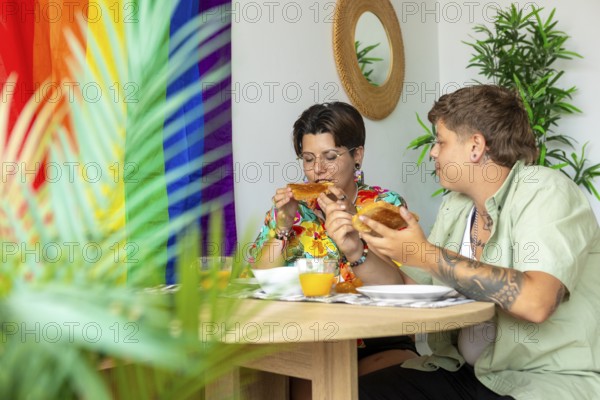 Lesbian couple enjoy breakfast at a wooden table adorned with orange juice, bread, and plates. A