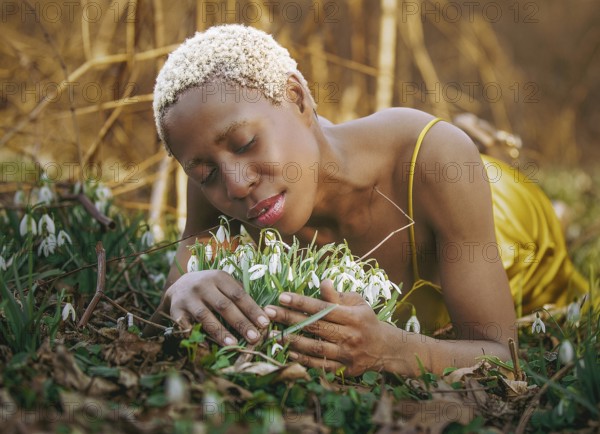A woman in a golden dress lies peacefully among blossoming snowdrops, enjoying nature tranquility