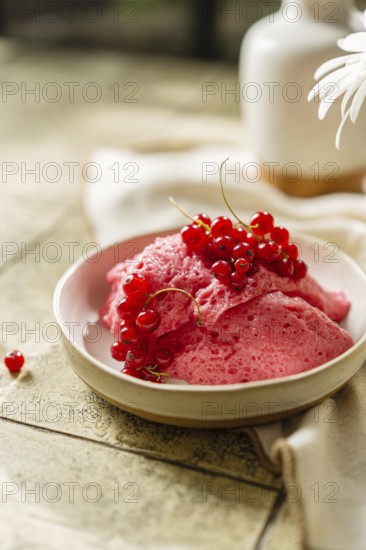 Homemade pink berry mousse garnished with fresh red currants in a ceramic bowl on a tiled table,
