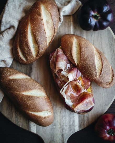 Freshly baked olive oil bread topped with slices of serrano ham and ripe tomatoes on a rustic