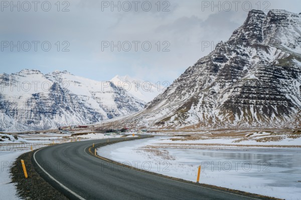 A curved road leads through stunning snowy mountains in Iceland. The winter landscape features