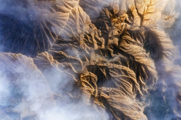 An aerial view showcases rocky mountain formations with deep ridges and valleys Wisps of mist