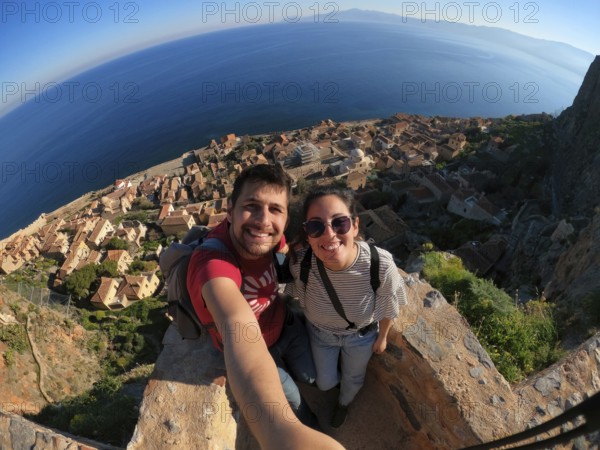 A joyful couple takes a selfie overlooking the charming town and azure sea from the heights of