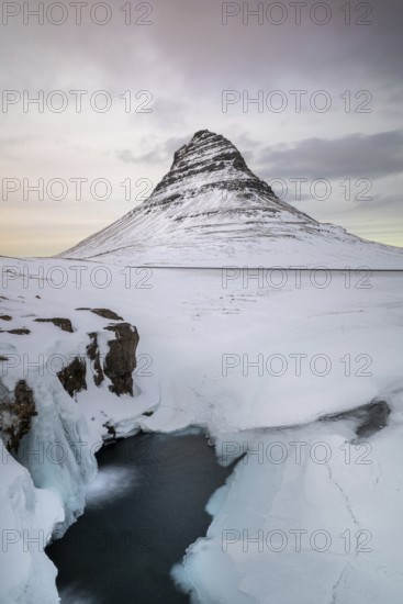 Kirkjufell Mountain, Iceland's iconic landmark, surrounded by a snowy landscape and icy waters,