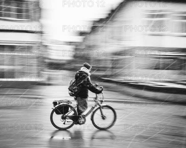 A person on a bicycle rides through a city in bad weather and sleet, rainy day black and white