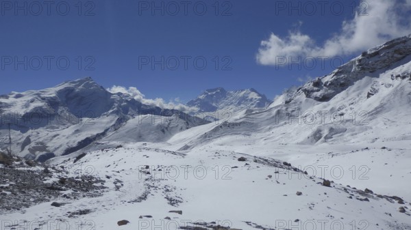 Clouds move across snowy mountain scenery on the way to Thorong La Pass, with rugged peaks and blue
