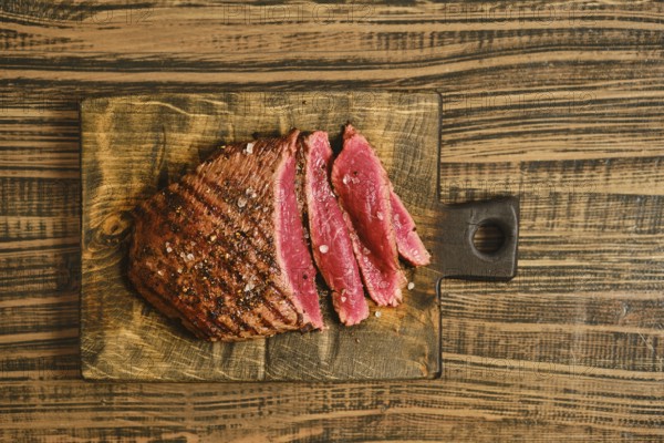 Beef is sliced into thick pieces and placed on a wooden cutting board. The meat shows a reddish