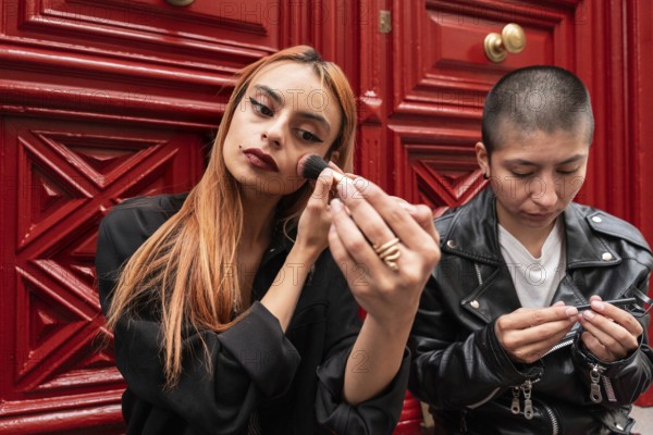 A lesbian couple enjoys a moment together, one applying makeup while the other engages in