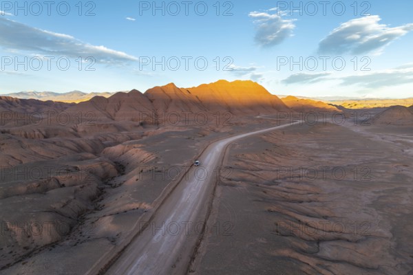 Aerial view of a vehicle in a empty desert road winding through rugged, sunlit mountains at dawn in