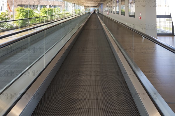 A modern airport travelator extends into the distance, surrounded by glass walls and natural light.