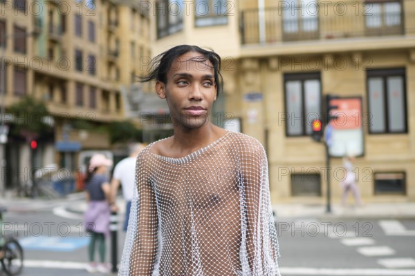 A confident man wearing a mesh top stands on a city street, embodying pride and LGBTQIA+ identity.