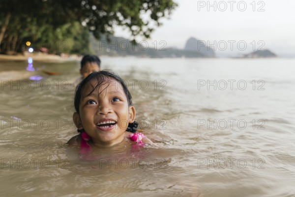 Two children enjoy swimming in the warm, shallow waters of a beach in the Philippines, surrounded