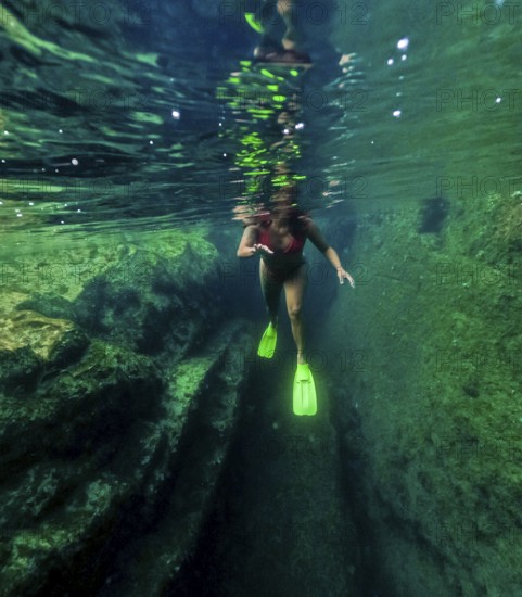 Underwater view of a woman with flippers snorkeling in the crystal clear waters of a natural pool