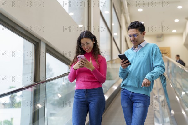 Young man and woman, Gen Z friends, enjoy using their smartphones while riding an escalator in a