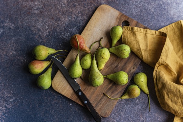 A collection of wild pears is artfully arranged on a rustic wooden cutting board. The setting