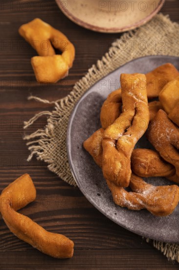 Crunchy biscuit Brushwood cookies sprinkled with powdered sugar on brown wooden background and