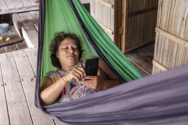 A mature woman enjoys a tranquil moment in a vibrant green hammock on Kri Island, Raja Ampat, while