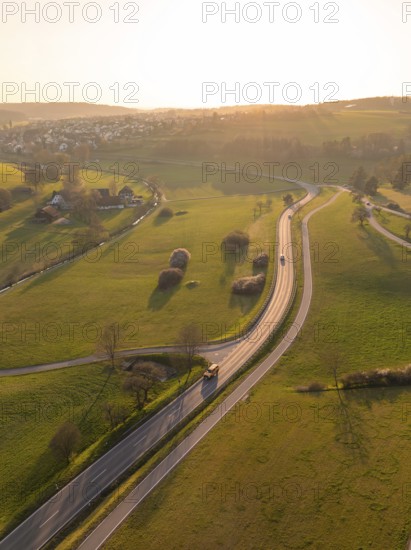 Winding country road through green fields and trees, under a warm sunset sky, Gechingen, district