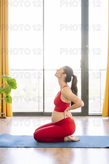 A pregnant woman practices yoga in a serene setting, embracing wellness and relaxation. She kneels