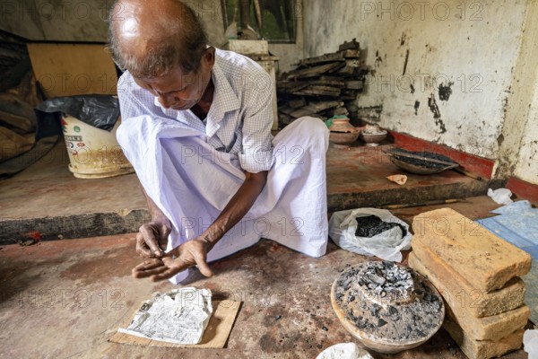 A man is busy with coal and a newspaper clipping in a quiet workshop, a man is burning sapphires in