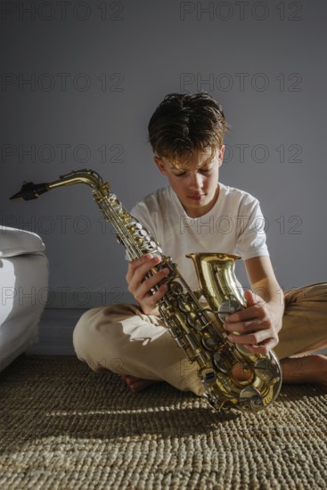 A young musician sits indoors in soft natural light, examining a saxophone. The scene captures