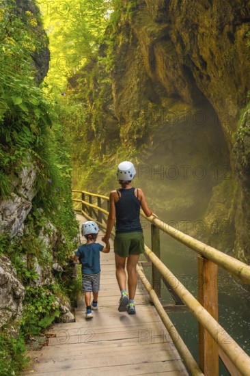 Mother and son wearing helmets are walking on a wooden walkway, exploring the beautiful vintgar