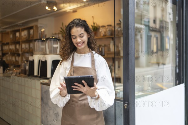 A smiling clerk wearing an apron uses a tablet to manage inventory at an organic bulk store.