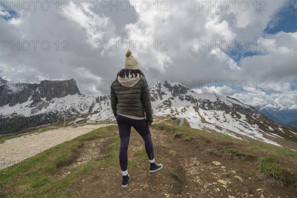 A woman stands at Passo Giau in the Dolomites, Italy, gazing at the snow-covered mountains under