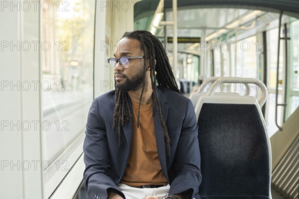 A cuban business man sits thoughtfully on a modern tram, gazing out the window. The serene