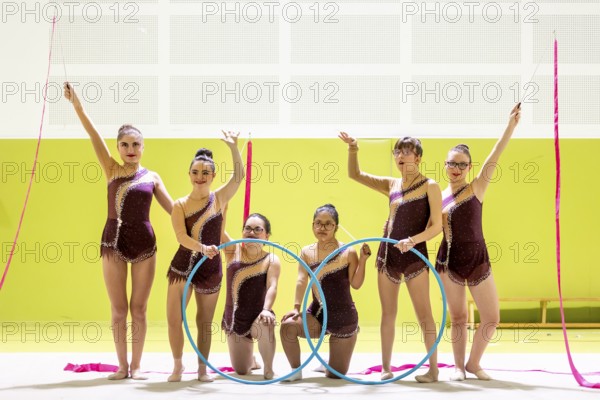 Group of gymnasts whit disability in maroon outfits performing with hoops and ribbons in a brightly