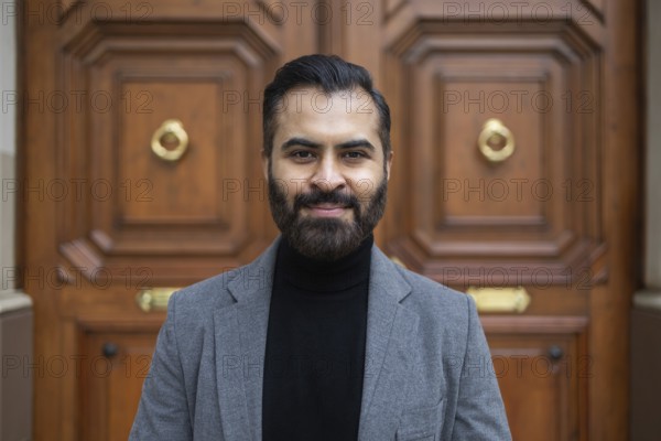 Portrait of a confident Indian businessman in a grey coat and black turtleneck, standing in front