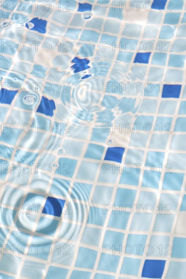 A close-up image of mosaic tiles under clear, rippling water, creating a serene and refreshing