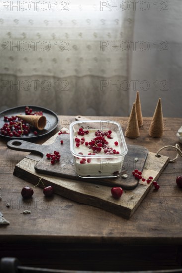 Rustic scene of homemade vanilla ice cream garnished with red currants and berries, served on a