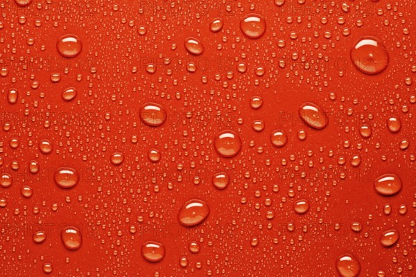 Close up of water droplets on a bright red surface, capturing the texture and varying sizes of the