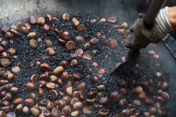 Close-up view of a cropped unrecognizable person roasting fresh chestnuts in a large pan at a Hong