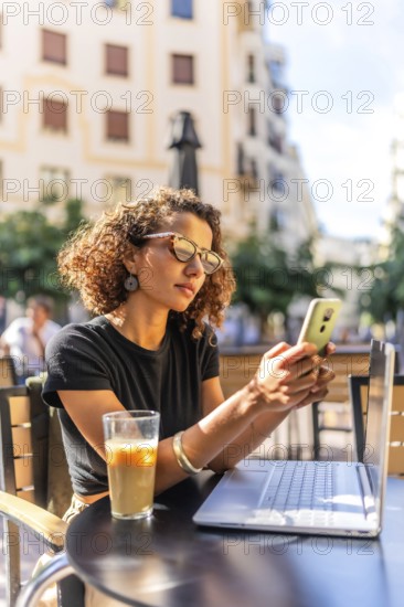 Vertical photo of a young Moroccan female freelancer working with mobile and laptop in a sidewalk
