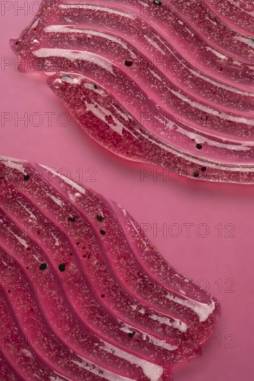 A detailed view of pink scrub and cosmetic gel, elegantly smeared on a pink surface, showcasing the